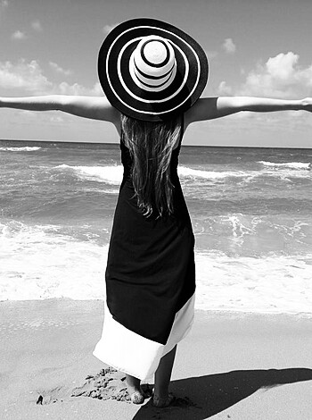 A naked broad with tits spinnin’ ass on the sandy shore in some sorta woven hat while sporting a dumb-ass dress that won’t stay on when the wind picks up like a fuckin’ gusty gust.