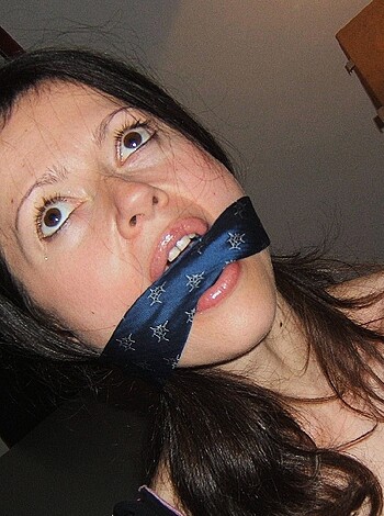 """
This image features a bitch who's got her mouth covered with a fucking rag while she's also wearing some dumbass T-shirt, and she's got a goddamn tie choking the life out of her. It's fucking disgusting!
"""