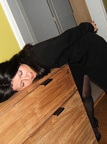 "Here's a picture of some hot chick in a black dress with stockings showing through her skirt, leaning over a wooden chest while taking a break from fucking."