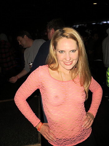 "Busty blonde bitch flashin' her titties & dyke ass in a pink tee while grinnin' like she wants to fuck the whole crowd."