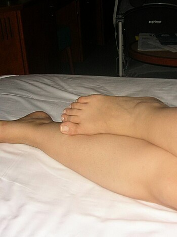 A naked ass is lying on a fluffy comforter with its toes curled up and touching the smooth white sheets underneath.
