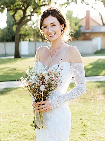 A busty blonde babe in a wedding gown grinning like a ditz, with a huge ass and tits, clutching some white roses.