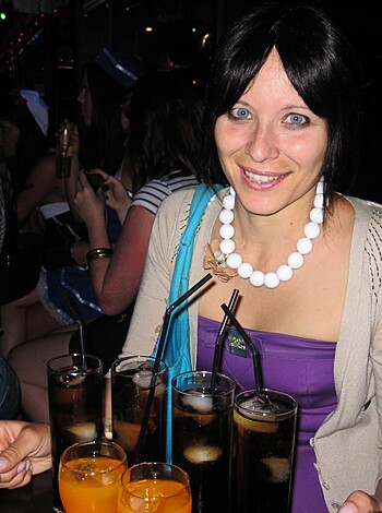 A chick with tits hanging out of her purple shirt, grinning while balancing multiple booze-filled tumblers on a tray like a boss bitch at the bar.