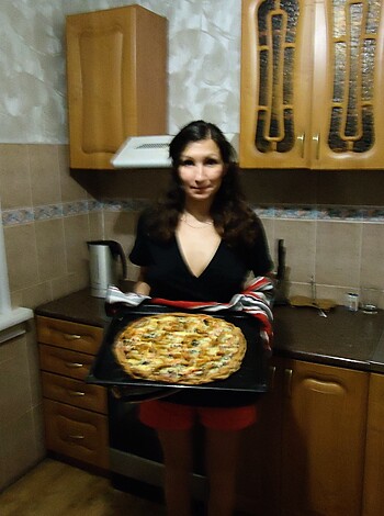 A fuckin hot bitch squeezin her ass while holdin up some goddamn pizza in a fuckin kitchen.