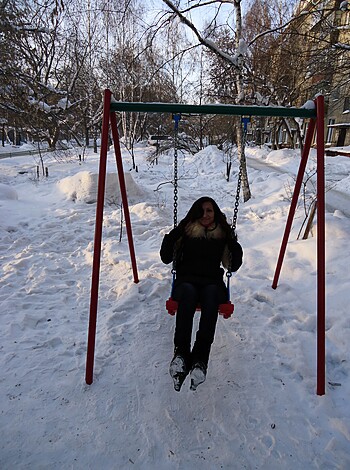 A fucking bitch chick sits on a swings with snow all around the fucking place.