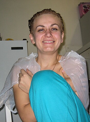 A bitch strips down and covers herself with plastic sheeting while sitting on her ass in a kitchen.