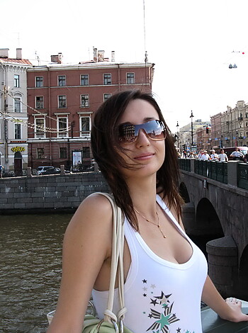 This chick is standing on a fuckin' green bridge, wearing a white tits-top and some dumb shades, while she's gazin' at some boring-ass canal in the background.