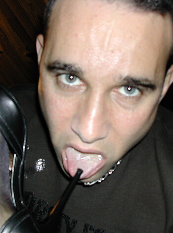 A guy holding his black shoe up to his lips, about to kiss it with a wink and smile on his face.