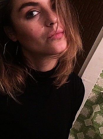 A naked bitch with huge tits is showing off her pierced nipples while flaunting a tight ass through a see-through panty, looking at the camera with a sexy smirk on her face.
