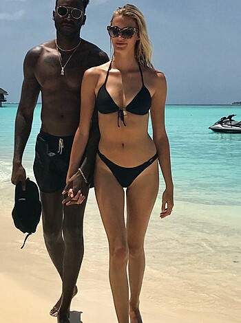 The photo shows a scantily clad male and female strutting their asses on the sandy shore.