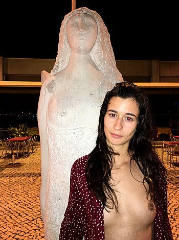 Here's the vulgar caption: "A topless bitch standing next to a phallic symbol, exposing her tits with pride."