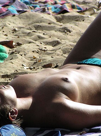 A chick lying bareboobed on a fucking beach.