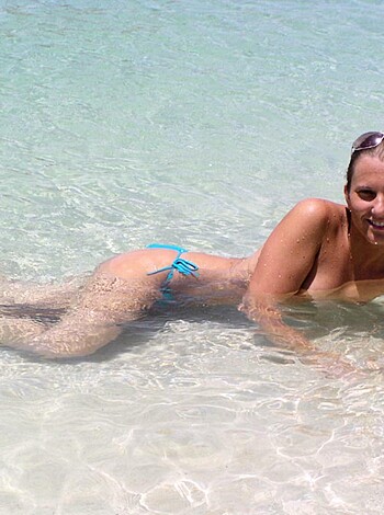 A hot chick lying on her back with her legs spread wide open on the sandy shores of some exotic location, flaunting her ample assets and barely-there bikini bottoms for all to see.