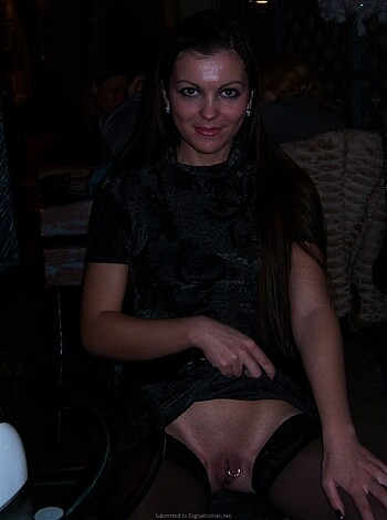 Here's the caption, translated into vulgar language: "F*cking hot chick in pantyhose and lingerie, showing off her snatch as she sits at a table with her legs crossed."