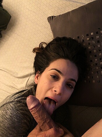 A naked female is giving head to some dick, as she lays flat on the bed.