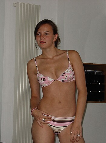 A scantily clad chick with pink nipples and white string bikini bottoms strikes a pose on the beach.