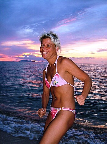 A chick in a pink two-piece struts her stuff on the sandy shore, as the sun dips below the horizon.